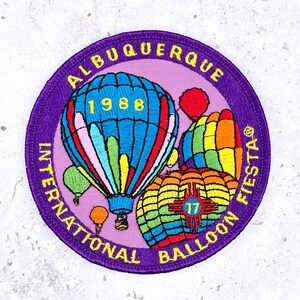 May include: Embroidered patch with a purple border and a light purple center. The patch features colorful hot air balloons and the text "Albuquerque International Balloon Fiesta 1988".