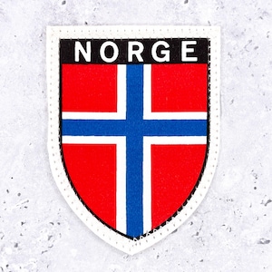 May include: A shield-shaped patch featuring the flag of Norway with a red background, a blue cross, and white borders. The word NORGE is printed in white capital letters on a black horizontal bar at the top. The patch has a white stitched border.