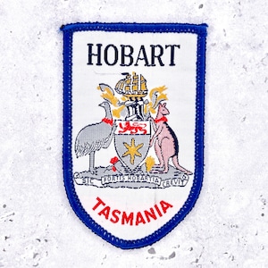May include: A white patch with a blue border featuring the word "HOBART" at the top and "TASMANIA" at the bottom in red. The patch includes a coat of arms with an emu, kangaroo, ship, and shield.