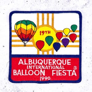 May include: Embroidered patch featuring a colorful hot air balloon and smaller balloons. The patch reads "Albuquerque International Balloon Fiesta 1990" in white text on a red background, with a blue border.