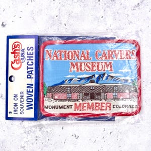 Puede incluir: Un parche de recuerdo tejido de Cash's USA, con el Museo Nacional de Talladores en Monument, Colorado. El parche tiene un borde rojo, un fondo de cielo azul y una representación del edificio del museo y las montañas. El texto dice "MEMBER" y "COLORADO".