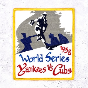 May include: Embroidered patch featuring a baseball player in action, with the text "World Series Yankees vs Cubs 1938." The patch has a white background, a yellow border, and a design in blue, red, and gray.