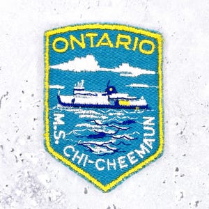 May include: Embroidered patch in a shield shape. It features the text "ONTARIO" in yellow above a blue image of a ferry boat on water. The text "M.S. CHI-CHEE-MAUN" is arched below. The patch has a yellow border.