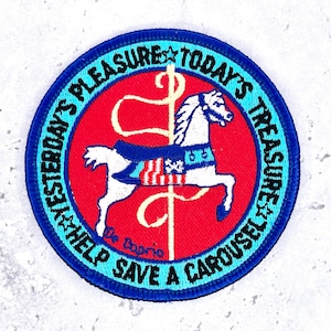 May include: A circular embroidered patch featuring a white carousel horse on a red background. The border is bright blue with the text YESTERDAY'S PLEASURE TODAY'S TREASURE HELP SAVE A CAROUSEL and the name De Caprio in black lettering.