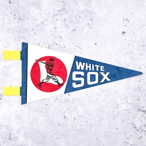 May include: A pennant-shaped White Sox baseball team flag. The flag is white with a blue triangle on the right side, displaying the team name. A red circle on the left features a baseball player illustration. Yellow tabs are attached.