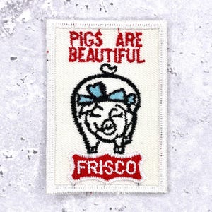 Peut inclure: Écusson rectangulaire à fond blanc et bordure rouge. Le patch présente le texte "PIGS ARE BEAUTIFUL" en rouge, au-dessus d'un cochon souriant avec un nœud bleu. En dessous du cochon se trouve le mot "FRISCO" en rouge.