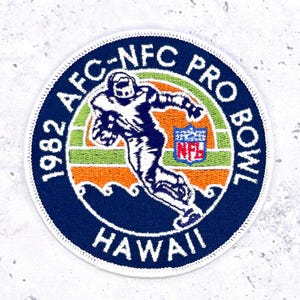 May include: A circular patch with the text "1982 AFC-NFC PRO BOWL HAWAII" in white lettering on a navy blue background. The patch features a football player graphic in white and navy blue, with orange, green, and blue accents. The NFL logo is also visible.