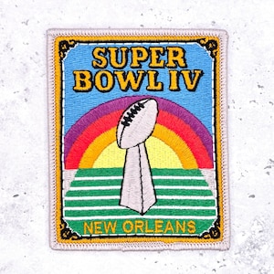 May include: Embroidered patch featuring the text "SUPER BOWL IV" above a rainbow and a football trophy. The patch also includes the text "NEW ORLEANS" at the bottom. The patch has a blue background with a gold border.