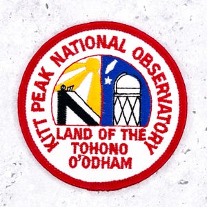 May include: Embroidered patch with a red border and white background. The patch features the text "KITT PEAK NATIONAL OBSERVATORY" and "LAND OF THE TOHONO O'ODHAM". The center design includes a sun, a telescope, and a stylized "K" shape.