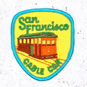 May include: A white ceramic mug with a black handle and the text "But First, Coffee" in a bold, black font. The mug is set against a blurred background, highlighting its clean design.