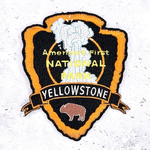 May include: Embroidered patch featuring the text "America's First National Park YELLOWSTONE". The patch has a black background with an orange border and a bison graphic. The text is in yellow and white.