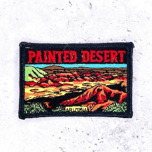 May include: Embroidered patch featuring the words "Painted Desert" in red letters above a colorful desert landscape. The patch includes the word "Arizona" at the bottom, with a black border.
