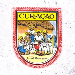 May include: A colorful patch featuring the word "CURAÇAO" in yellow, with an illustration of a local music group. The patch has a red border and the text "Local Music group" at the bottom.