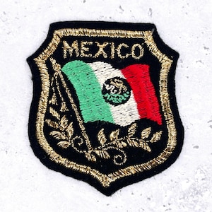 Könnte beinhalten: Gestickter Aufnäher mit der mexikanischen Flagge in Schildform. Der Aufnäher hat einen schwarzen Hintergrund mit goldenem Rand und dem Wort "MEXICO" oben. Die Flagge zeigt grüne, weiße und rote Streifen mit dem mexikanischen Wappen.