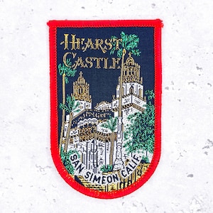 May include: A rectangular patch with a red border and a navy blue background. The patch features an embroidered image of Hearst Castle with the text "HEARST CASTLE" and "SAN SIMEON CALIF."