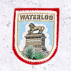 May include: Embroidered patch with a red border and gold trim. The patch features the word "WATERLOO" in gold lettering above an image of a lion statue atop a monument against a blue sky background.