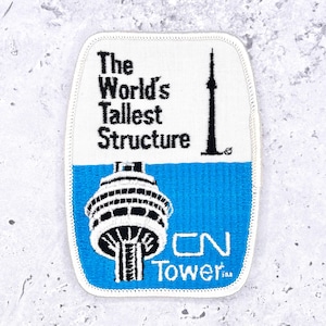 Op de afbeelding: Geborduurde patch met de CN Tower, een zwart-wit illustratie van de toren, en de tekst "The World's Tallest Structure". De patch heeft een witte achtergrond met een blauw onderste gedeelte en de tekst "CN Tower".