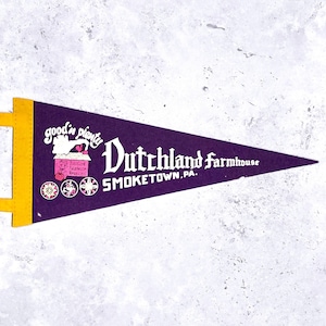 May include: A purple felt pennant with a yellow border and a white background. The pennant features the text "Dutchland Farmhouse SMOKETOWN, PA." and an illustration of a pink building with the words "good 'n plenty".