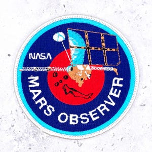 May include: Embroidered patch featuring the NASA logo and the words "MARS OBSERVER" in white lettering on a blue background. The patch includes a red circle with a detailed illustration of a spacecraft and solar panels.