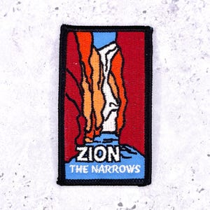 Op de afbeelding: Geborduurde patch met een gestileerd landschap van Zion National Park's The Narrows. Het ontwerp bevat rode, oranje en witte rotsformaties tegen een rode achtergrond, met een blauwe lucht en de tekst "ZION THE NARROWS". De patch heeft een zwarte rand.