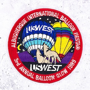 May include: Embroidered patch with a red border featuring text: "ALBUQUERQUE INTERNATIONAL BALLOON FIESTA" and "3rd ANNUAL BALLOON GLOW 1989." The patch depicts two hot air balloons, a howling wolf, and the text "US WEST."