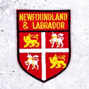 May include: A red, shield-shaped patch with the words "NEWFOUNDLAND & LABRADOR" in yellow. The patch features a white cross and four quadrants with yellow lions and white unicorns.