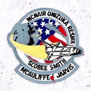 May include: A circular embroidered patch featuring a space shuttle with a yellow exhaust trail, a blue and grey globe, and a red, white, and blue American flag. The text reads MCNAIR ONIZUKA RESNIK SCOBEE SMITH MCAULIFFE JARVIS in black thread.