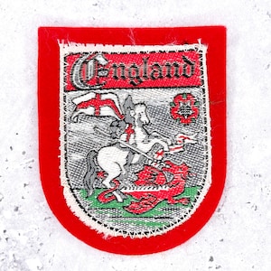 May include: A shield-shaped embroidered patch with a bright red border. The center features a woven scene of a white horse and rider battling a red dragon, with the word England in black gothic lettering on a red background at the top.
