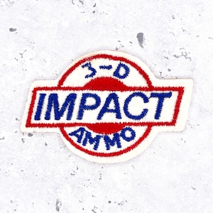 May include: A circular embroidered patch with a white background and a red border. The text 3-D is stitched in blue at the top. A central red horizontal bar features the word IMPACT in blue, with the word AMMO stitched in blue at the bottom.