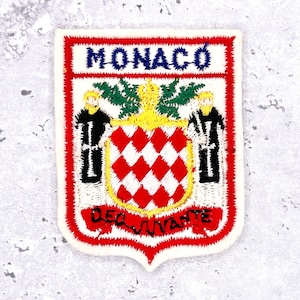Op de afbeelding: Geborduurde patch met het wapen van Monaco. De patch heeft een witte achtergrond met een rode rand. De tekst "MONACO" staat bovenaan en "DEO JUVANTE" onderaan. Het wapen bevat een rood-wit geblokt schild.