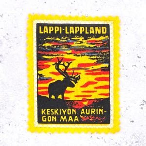 May include: A rectangular patch with a yellow scalloped border. The patch features a sunset scene with a black silhouette of a reindeer. Text at the top reads "LAPPI-LAPPLAND" and at the bottom "KESKIYON AURINKON MAA".