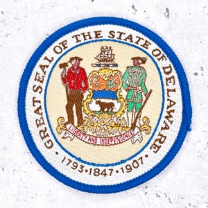 May include: Embroidered patch featuring the Great Seal of the State of Delaware. The circular patch has a blue border and includes text that reads "GREAT SEAL OF THE STATE OF DELAWARE" and "LIBERTY AND INDEPENDENCE". The patch also includes the years 1793, 1847, and 1907.