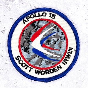 Może przedstawiać: Okrągła naszywka haftowana z niebieską obwódką i białym tłem. Centralny wzór zawiera elementy czerwone, białe i niebieskie. Tekst "APOLLO 15" i "SCOTT WORDEN IRWIN" jest w białych literach.