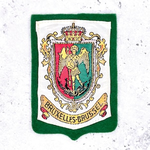 May include: A rectangular patch with a green border and a central emblem. The emblem features a coat of arms with a crown, a figure with wings, and the text "BRUXELLES-BRUSSEL" in a banner. The colors include red, green, gold, and white.