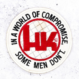 May include: A circular embroidered patch with a white background and a red border. The centre features a large red HK logo over a white grid pattern. Black text encircles the logo reading, IN A WORLD OF COMPROMISE, SOME MEN DON'T.