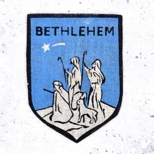 Può includere: Toppa blu e bianca con la scritta "BETHLEHEM" in alto. La toppa presenta una stella e una scena con figure e un cane, che probabilmente raffigura un evento religioso. La toppa ha un bordo nero.