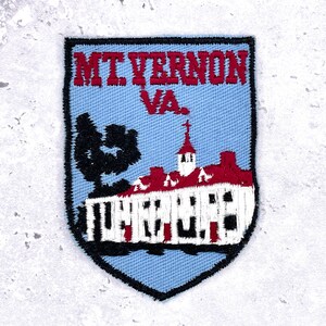 Op de afbeelding: Geborduurde patch met de tekst "MT VERNON VA." boven een wit gebouw met een rood dak en een zwarte boom. De patch heeft een lichtblauwe achtergrond en een zwarte rand.