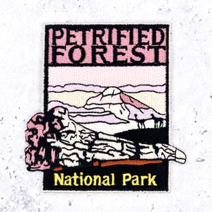 May include: A rectangular embroidered patch featuring the text PETRIFIED FOREST in black letters on a pink background. The design depicts a stylized landscape with a large piece of petrified wood in the foreground and the text National Park below.