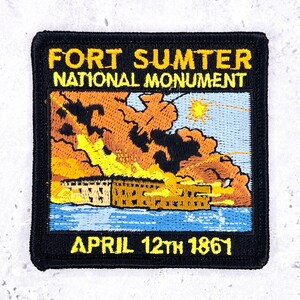 May include: A square embroidered patch with a black border. The top text reads FORT SUMTER NATIONAL MONUMENT in yellow. The center depicts a fort under fire with orange smoke and yellow flames over blue water. The bottom text reads APRIL 12TH 1861.