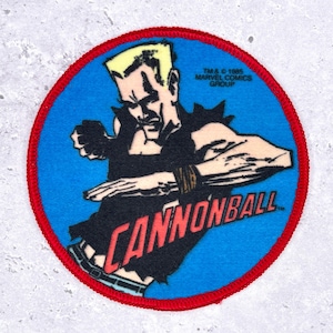 Op de afbeelding: Ronde patch met een stripboekillustratie van Cannonball, een personage van Marvel Comics. De patch heeft een blauwe achtergrond, een rode rand en de naam van het personage in het rood. De tekst "TM & © 1985 MARVEL COMICS GROUP" is ook zichtbaar.