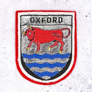 May include: Embroidered patch with the word "OXFORD" above a red bull on a shield. The shield has a blue wavy pattern at the bottom and is outlined in red, white, and black.