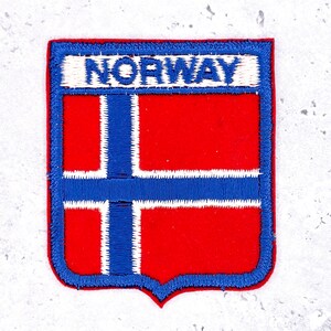 May include: Embroidered patch featuring the flag of Norway. The patch has a red background with a blue cross outlined in white. The word "NORWAY" is embroidered in white on a blue banner at the top. The patch is bordered in blue.