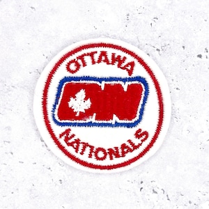 May include: A circular patch with the words "OTTAWA NATIONALS" in red, surrounding a red and blue emblem. The emblem features a white maple leaf and the letters "ON".