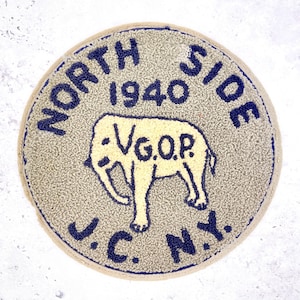 May include: Circular patch with a textured, light grey background and a navy blue border. The text "NORTH SIDE 1940" arches across the top. A light yellow elephant graphic is in the centre, with "V.G.O.P." below it. The text "J.C. N.Y." is at the bottom.