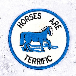 Peut inclure: Un écusson brodé circulaire avec un fond blanc et une bordure bleue. L'écusson représente un cheval bleu avec une crinière et une queue blanches, accompagné du texte brodé noir "HORSES ARE TERRIFIC" arqué autour du cheval.
