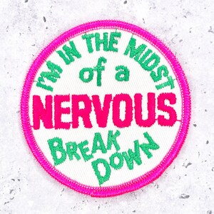 May include: Round embroidered patch with a white background and a hot pink border. The patch features the text "I'M IN THE MIDST of a NERVOUS BREAK DOWN" in green and pink lettering.