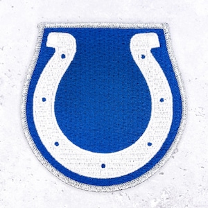 May include: A blue and white patch featuring the Indianapolis Colts horseshoe logo. The patch has a blue background with a white horseshoe in the center. The patch is bordered with a silver metallic thread.