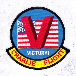May include: Embroidered patch with a blue background and a black border. The patch features a red "V" over a stylized American flag. The text "VICTORY!" and "CHARLIE FLIGHT" are in yellow.