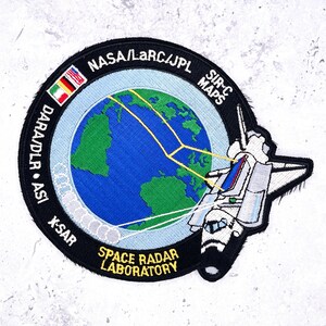 May include: Embroidered patch featuring a detailed design with a blue and green globe, a space shuttle, and text that reads "NASA/LaRC/JPL" and "SPACE RADAR LABORATORY". The patch has a black border and includes flags.