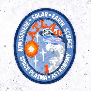 Peut inclure: Écusson brodé avec une bordure ovale bleue. Il présente le mot "ATLAS" et les phrases "Atmosphère", "Solaire", "Science de la Terre", "Plasma spatial" et "Astronomie". Il comprend un soleil stylisé, une fusée et des étoiles.